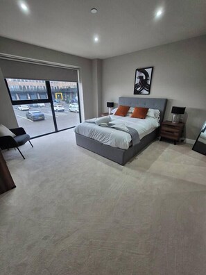 A modern bedroom with a large bed, a chair, a desk, and a view of the parking lot through a sliding door. - #22 Lux Apart balcony 11|Near NEC & BHX|for 4 (Birmingham)