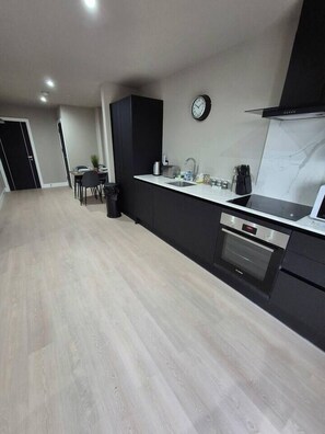 A modern kitchen with a black countertop, stainless steel appliances, and a dining area with a table and chairs. - #22 Lux Apart balcony 11|Near NEC & BHX|for 4 (Birmingham)