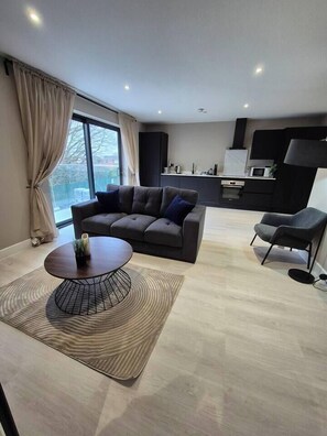 A modern living room with a sofa, a coffee table, and a chair. There is a kitchen area in the background with cabinets and a microwave. - #23 Lux Flatbalcony|10mins to ResortsWorldBHM|for4 (Birmingham)