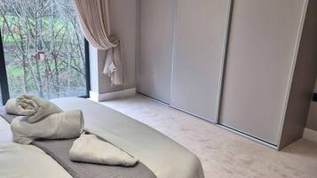 A modern bedroom with a large bed, a view through a window, and a sliding door.