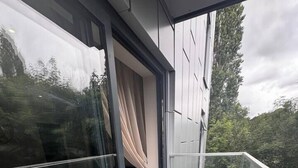 Parveke, jossa on lasiovi, kaksi tuolia ja näkymä puistoon.
