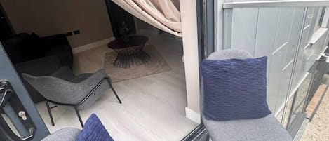 Un balcón con dos sillas grises, una con cojín azul, y un ventanal con cortinas.