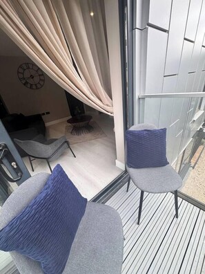 A balcony with two grey chairs, one with a blue cushion, and a glass door with curtains. - #23 Lux Flatbalcony|10mins to ResortsWorldBHM|for4 (Birmingham)