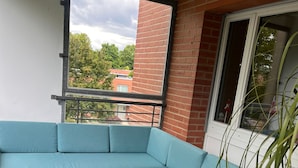 Uma varanda com um sofá azul em formato de L, uma mesa de madeira e um vaso com planta.