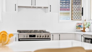 A modern kitchen with white cabinetry, a gas stove, and a window with a decorative view. - Zuri Luxury Coastal Staycation• 2 Min to Beach, Cafés & Lakefront (The Entrance)