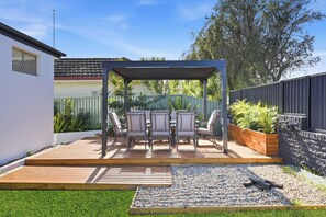 A patio with a pergola, outdoor furniture, and a garden area with pebbles and plants. - Zuri Luxury Coastal Staycation• 2 Min to Beach, Cafés & Lakefront (The Entrance)