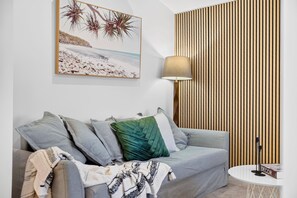 Una sala de estar moderna con un sofá gris, una lámpara decorativa, un panel de pared de listones de madera y un cuadro con temática de playa.