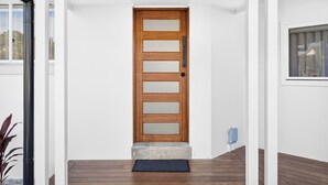 A wooden door with frosted glass panels, a doormat, and a small step leading to a wooden deck. - Zuri Luxury Coastal Staycation• 2 Min to Beach, Cafés & Lakefront (The Entrance)