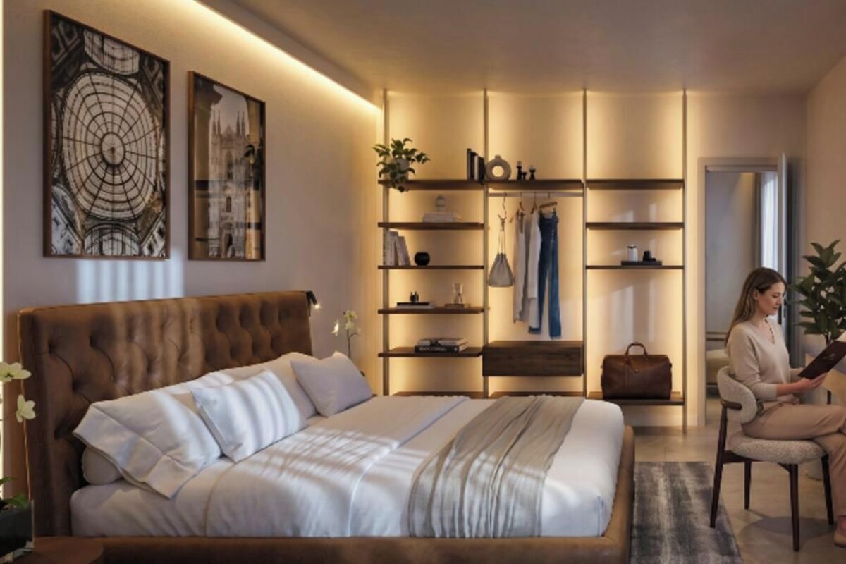 Ein modernes Schlafzimmer mit einem großen Bett, einer Sitzecke und einem Schreibtisch. Es gibt Regale mit Gegenständen und eine Pflanze.