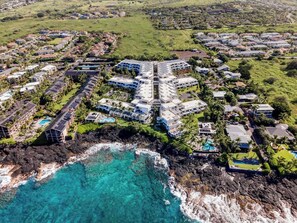 An aerial view of a coastal resort with multiple buildings, a rocky shoreline, and clear blue waters. - Honu Family Retreat Royal Seacliff#401 (Kailua Kona)
