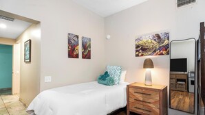 Una camera d'albergo con un letto, un comodino, una lampada, una TV e opere d'arte alle pareti.