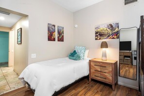 Ein Hotelzimmer mit Bett, Nachttisch, Lampe, Fernseher und Kunstwerken an den Wänden.