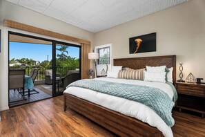 A bedroom with a large bed, a sliding glass door to a balcony, a ceiling fan, and a view of greenery. - Honu Family Retreat Royal Seacliff#401 (Kailua Kona)