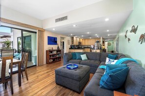 Ein modernes Wohnzimmer mit einem grauen Ecksofa, Holzboden und einem Essbereich mit Tisch und Stühlen.