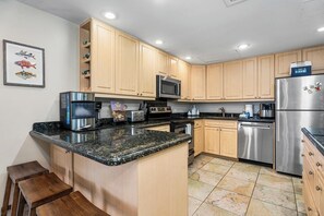 A modern kitchen with wooden cabinets, granite countertops, stainless steel appliances, and a built-in microwave. - Honu Family Retreat Royal Seacliff#401 (Kailua Kona)