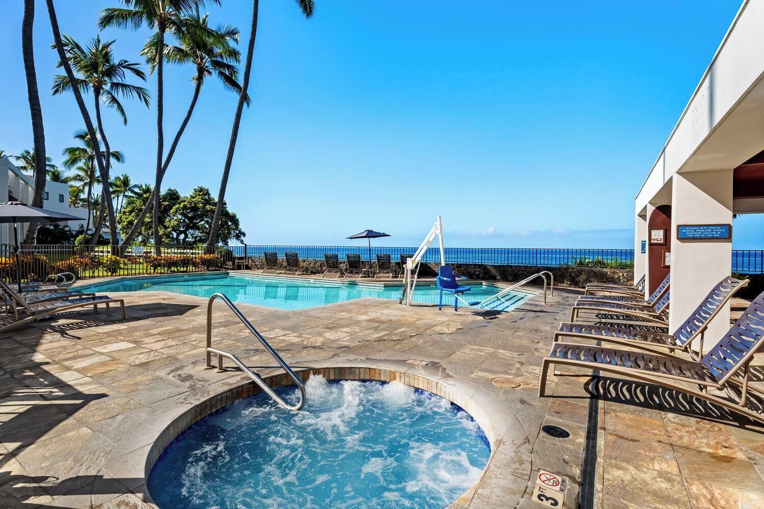 Un espace piscine doté d’un jacuzzi, de chaises longues et offrant une vue sur l’océan.