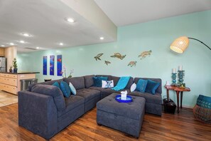 A modern living room with a grey sectional sofa, a coffee table, and a wall decorated with sea turtle decals. - Honu Family Retreat Royal Seacliff#401 (Kailua Kona)