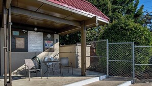 A covered outdoor seating area with a pool rules sign, a clock, and a fenced pool area. - Kona Mansions#B116 Mountain views, No Stairs, Heart of Town (Kailua Kona)