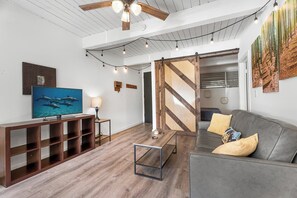 A modern living room with a television, a sofa, a coffee table, and a wooden entertainment unit. - Kona Mansions#B116 Mountain views, No Stairs, Heart of Town (Kailua Kona)