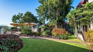 A well-maintained outdoor area with a lawn, a seating area with umbrellas, and a variety of plants and trees. - Kona Mansions#B116 Mountain views, No Stairs, Heart of Town (Kailua Kona)