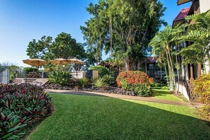 A well-maintained outdoor area with a lawn, a seating area with umbrellas, and a variety of plants and trees. - Kona Mansions#B116 Mountain views, No Stairs, Heart of Town (Kailua Kona)