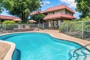 A swimming pool with a curved edge, surrounded by a fence, and adjacent to a building with a red roof. - Kona Mansions#B116 Mountain views, No Stairs, Heart of Town (Kailua Kona)