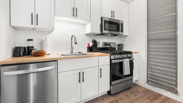 A modern kitchen with white cabinets, stainless steel appliances, and a wooden countertop. - Kona Mansions#B116 Mountain views, No Stairs, Heart of Town (Kailua Kona)