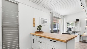 A modern kitchen with a wooden countertop, white cabinetry, and a small bonsai tree. - Kona Mansions#B116 Mountain views, No Stairs, Heart of Town (Kailua Kona)
