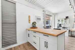 A modern kitchen with a wooden countertop, white cabinetry, and a small bonsai tree. - Kona Mansions#B116 Mountain views, No Stairs, Heart of Town (Kailua Kona)