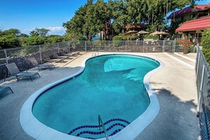 Una piscina de borde curvo, rodeada por una valla y protegida por sombrillas.