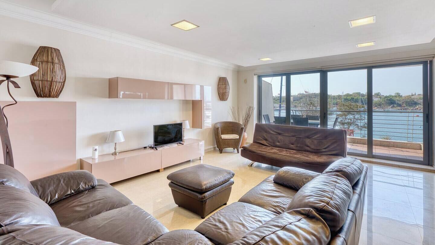 A modern living room with a large window, leather sofas, a flat-screen TV, and minimalist decor.