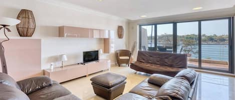 A modern living room with a large window, leather sofas, a flat-screen TV, and minimalist decor.