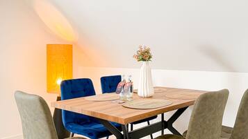 A dining area with a wooden table, blue upholstered chairs, a white vase with flowers, and a tall lamp.