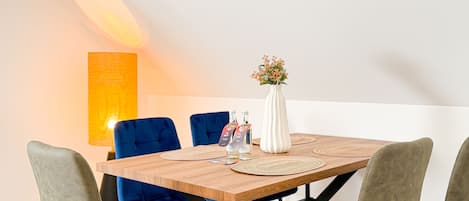 A dining area with a wooden table, blue upholstered chairs, a white vase with flowers, and a tall lamp.