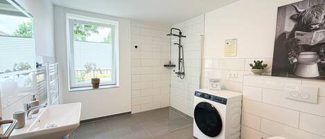 A modern bathroom with a shower, toilet, washing machine, and sink.