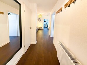 A hallway with a wooden floor, white walls, and a ceiling light fixture.