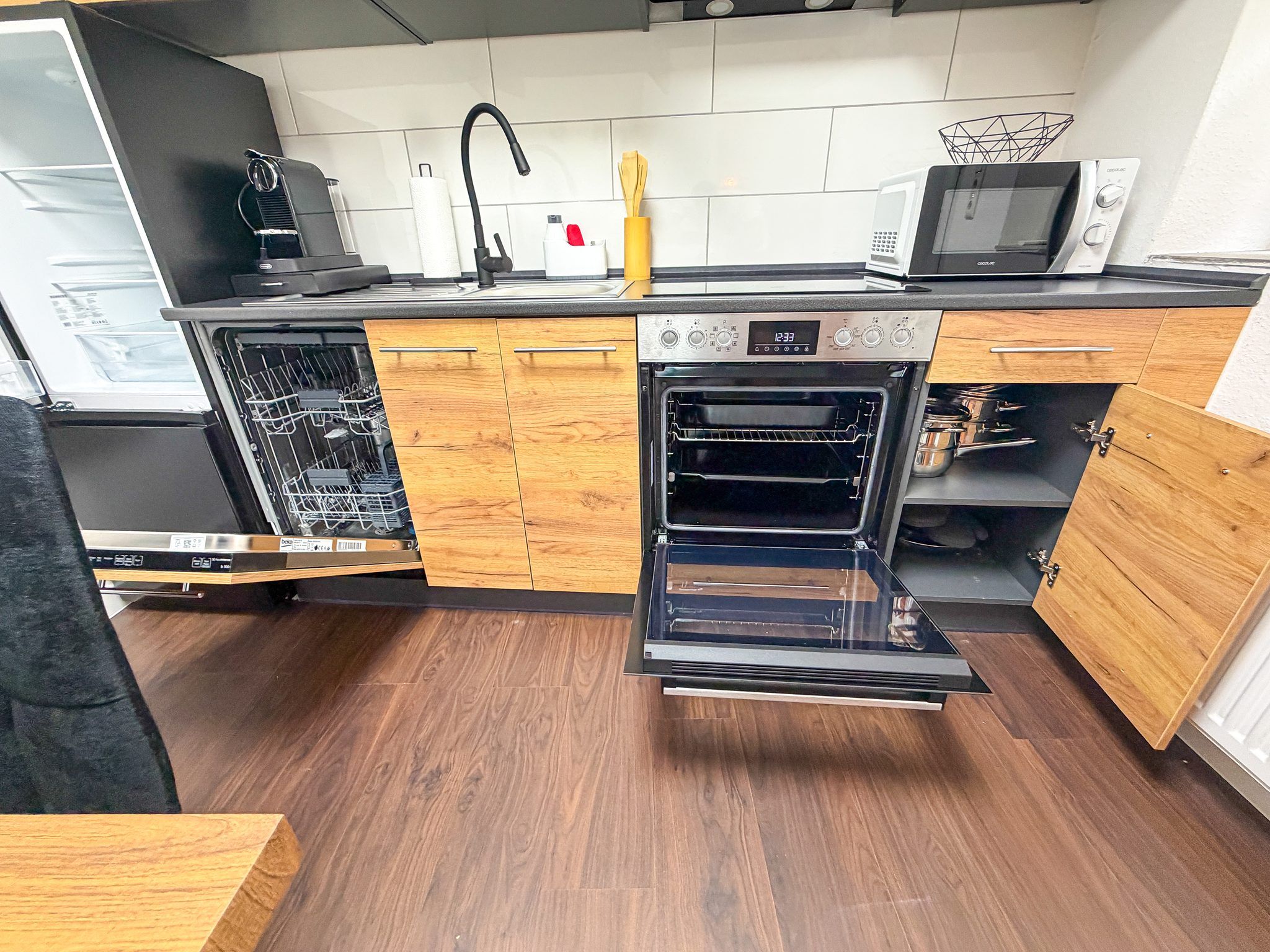 Cozinha compacta equipada com lava-louças, forno, micro-ondas e armários de madeira.