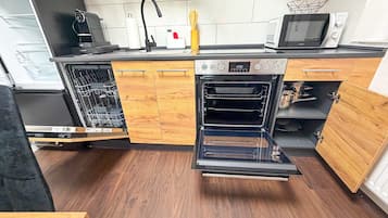Cozinha compacta equipada com lava-louças, forno, micro-ondas e armários de madeira.