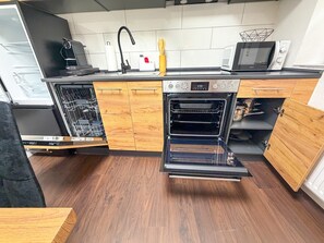 A compact kitchen with a dishwasher, oven, microwave, and wooden cabinetry.