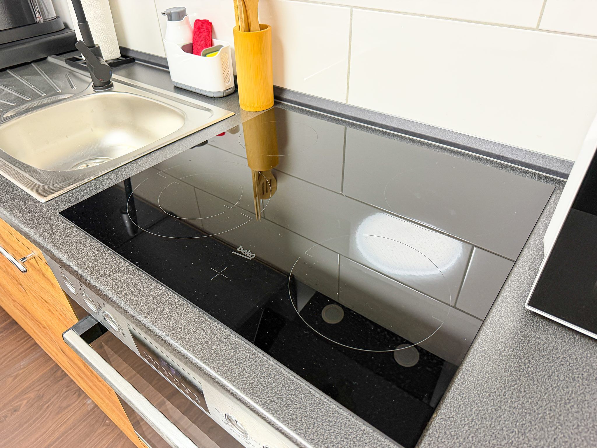 Et køkken med en sort induktionskogetop, en vask og en gul utensil holder.