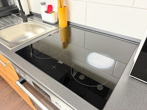 Een keuken met een zwart inductiekookveld, een spoelbak en een gele keukengerei houder.