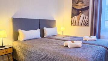 A hotel room with a large bed, two pillows, a nightstand with a lamp, and a painting on the wall.