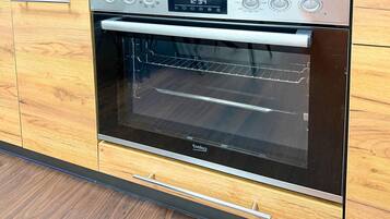 A modern kitchen with a built-in oven, wooden cabinetry, and a digital clock displaying the time.