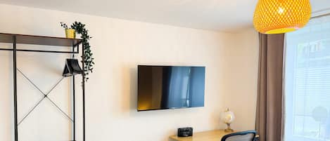 A modern room with a TV mounted on the wall, a desk with a chair, a bookshelf, and a bed with a patterned duvet.
