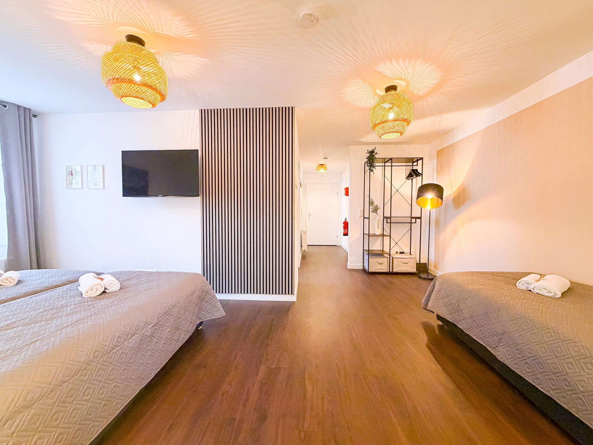 Hotellihuone, jossa on kaksi sänkyä, televisio, liukuovi ja käytävä, joka johtaa kylpyhuoneeseen.