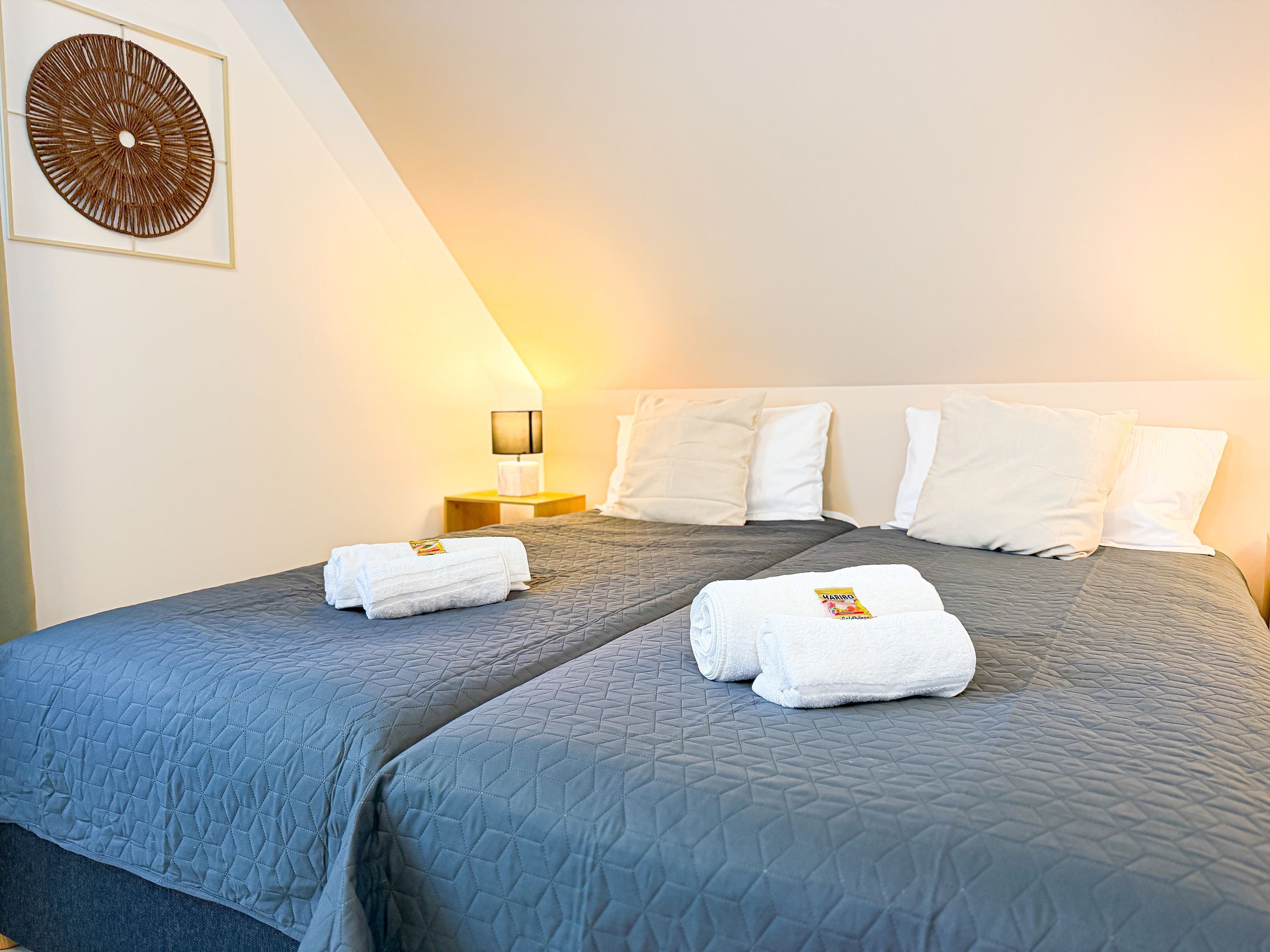 Quarto de hotel com uma cama grande, duas almofadas, uma mesa de cabeceira com abajur e uma obra de arte na parede.