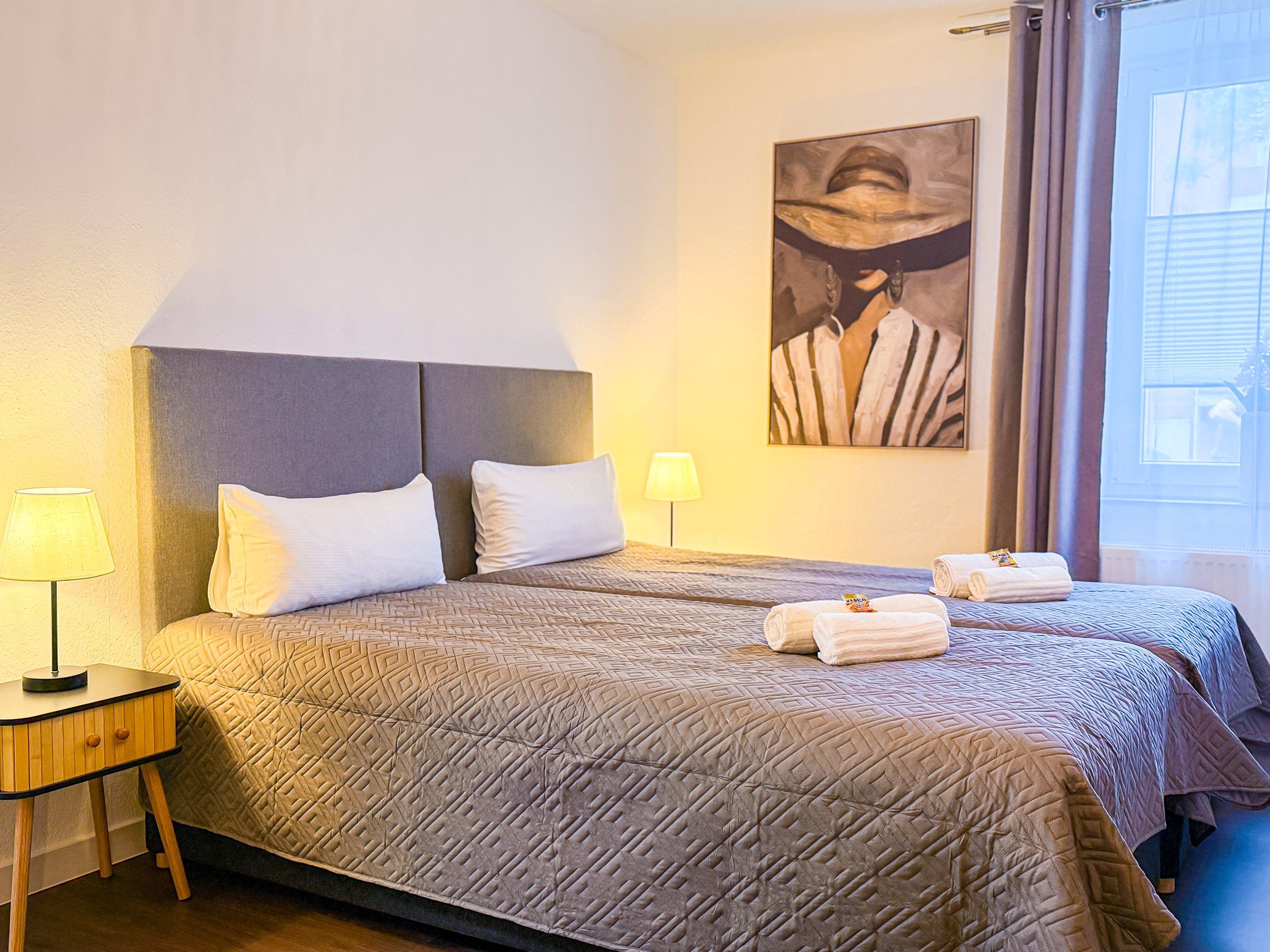 Habitación de hotel con una cama grande, dos mesitas de noche, una lámpara y un cuadro en la pared.