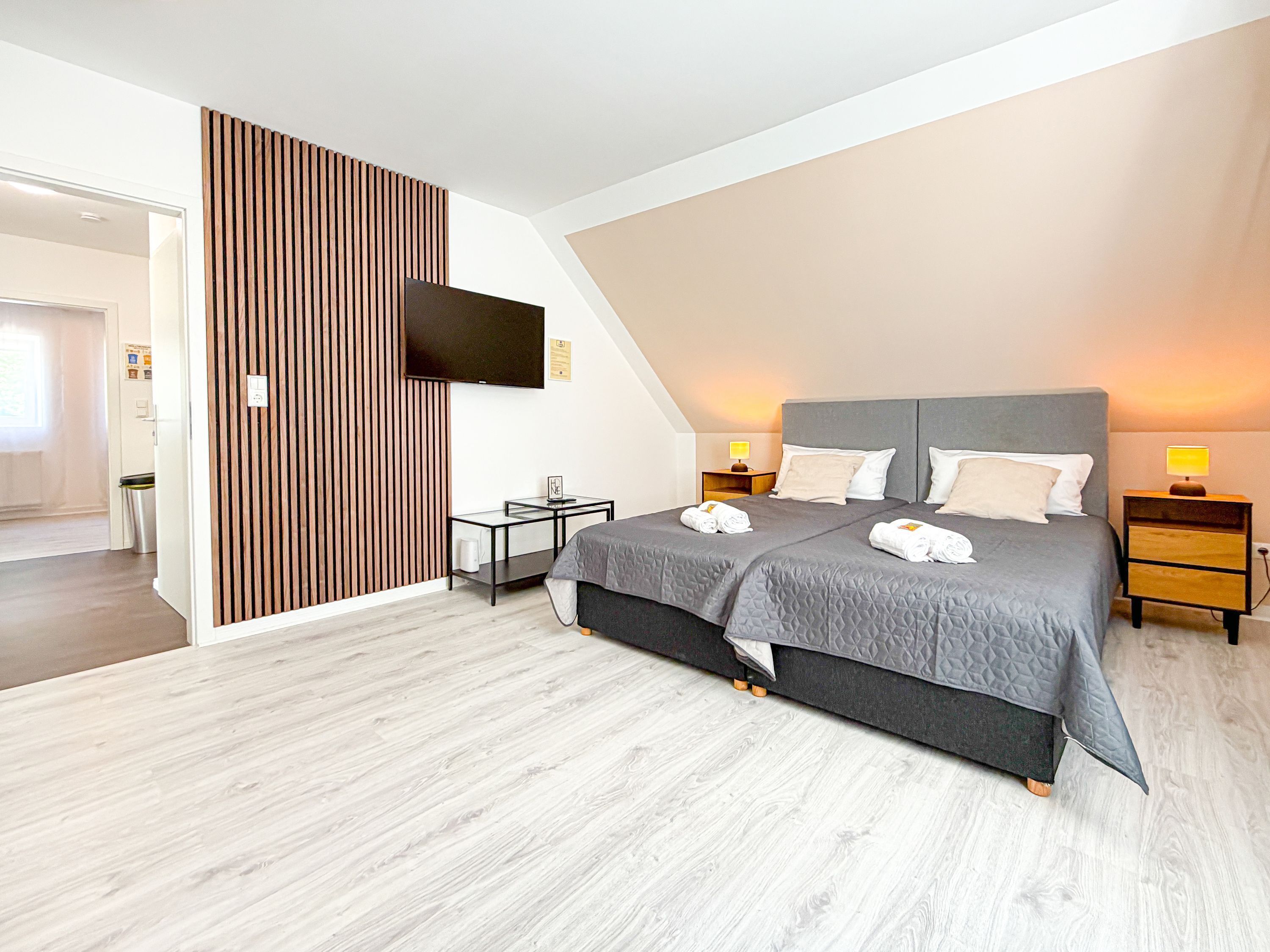 Un dormitorio moderno con una cama grande, mesitas de noche, un televisor y un panel de pared de madera.
