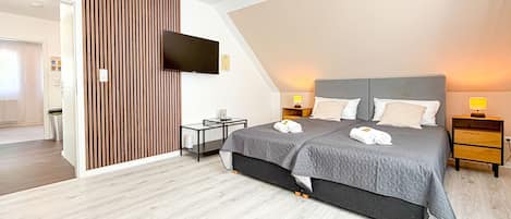 A modern bedroom with a large bed, bedside tables, a TV, and a wooden panel wall.