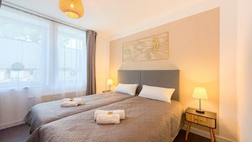 Ein Hotelzimmer mit zwei Betten, einem Nachttisch mit Lampe, einem Wandbild und einem Fenster mit Vorhängen.